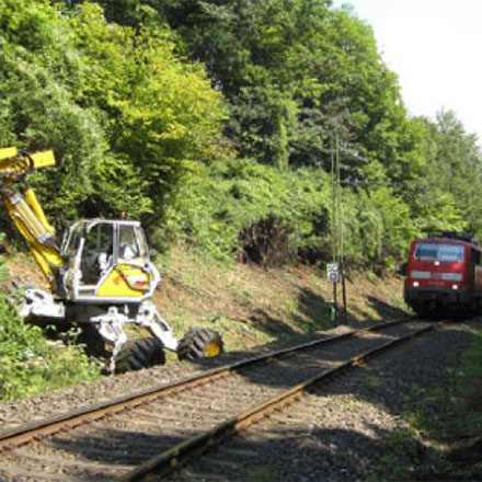 Schreitbagger mit Mulchkopf bei laufendem Bahnbetrieb